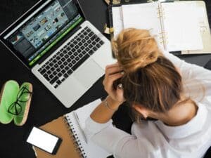 Overhead view of a stressed woman working at a desk with a laptop, phone, and notebooks.